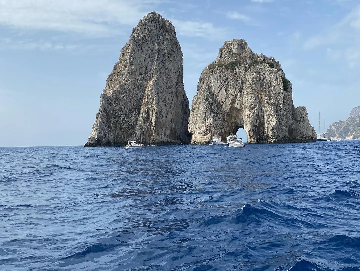 8BF9C5A6-1FC4-4268-A34F-66424BC8F353 Rock formations rise from the sea, with several boats nearby under a clear sky.