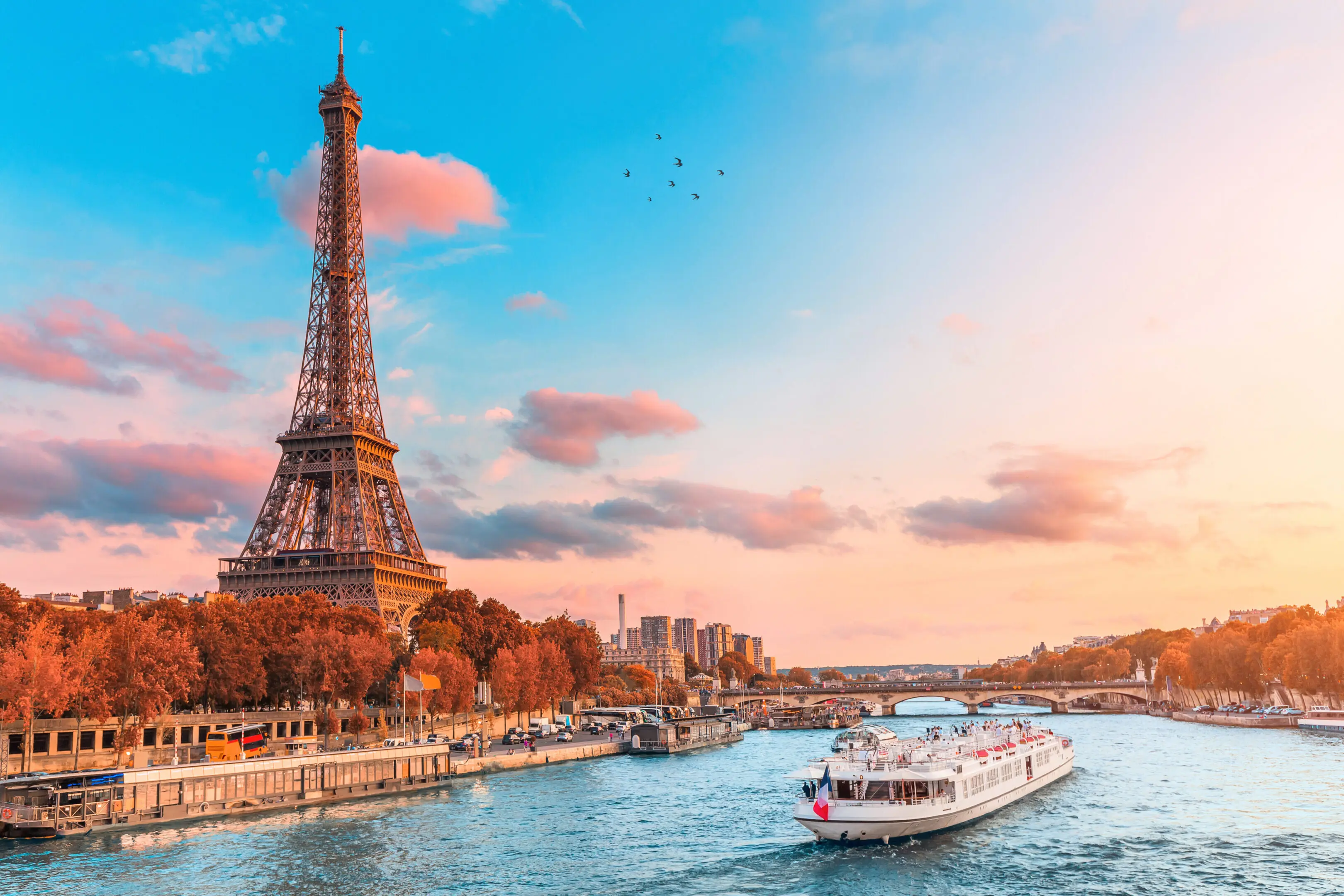 The main attraction of Paris and all of Europe is the Eiffel tower in the rays of the setting sun on the bank of Seine river with cruise tourist ships A boat is traveling down the river near the eiffel tower.