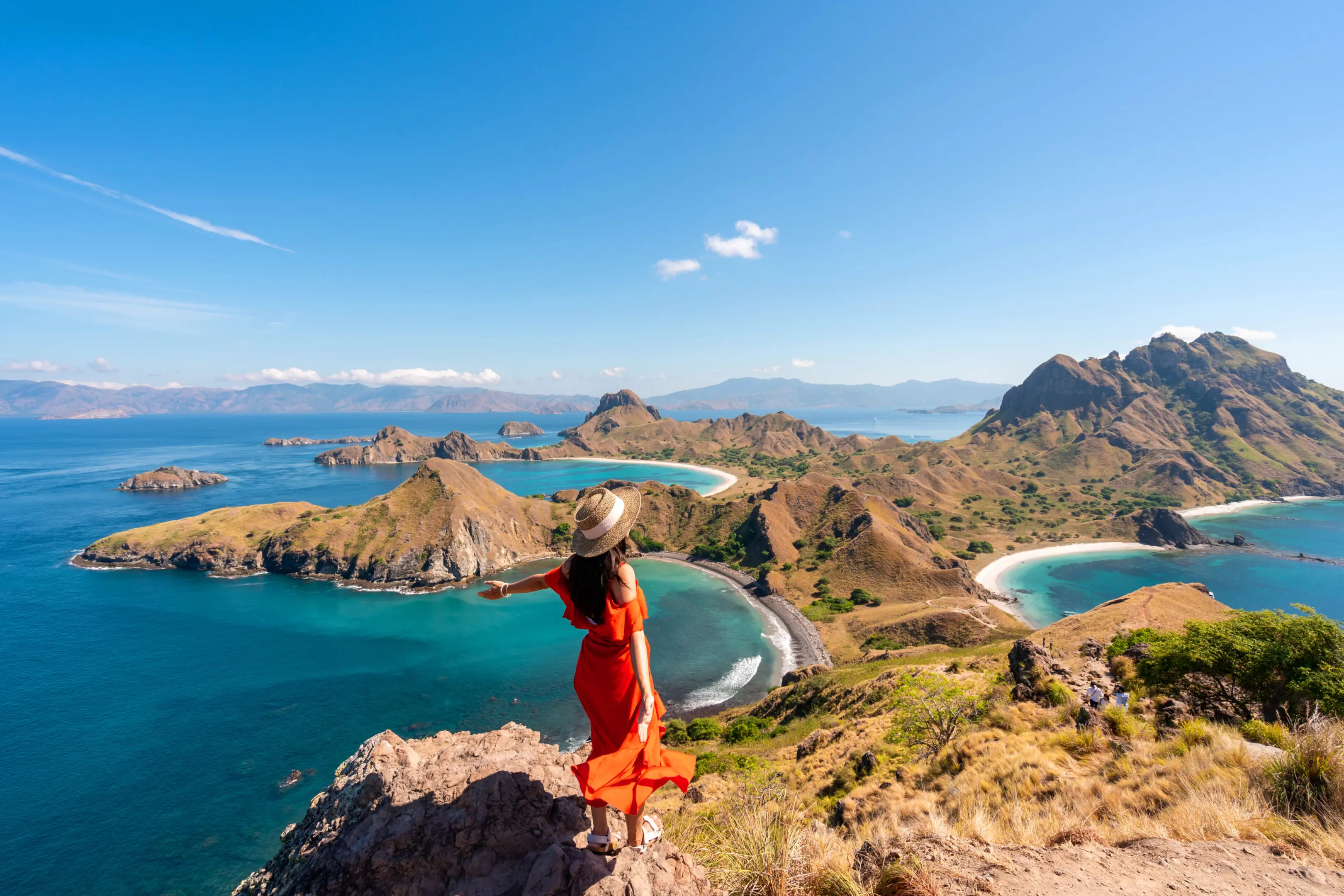 Young female tourist enjoying the beautiful landscape at Padar island in Komodo National Park, Indonesia A woman standing on top of a hill overlooking the ocean.
