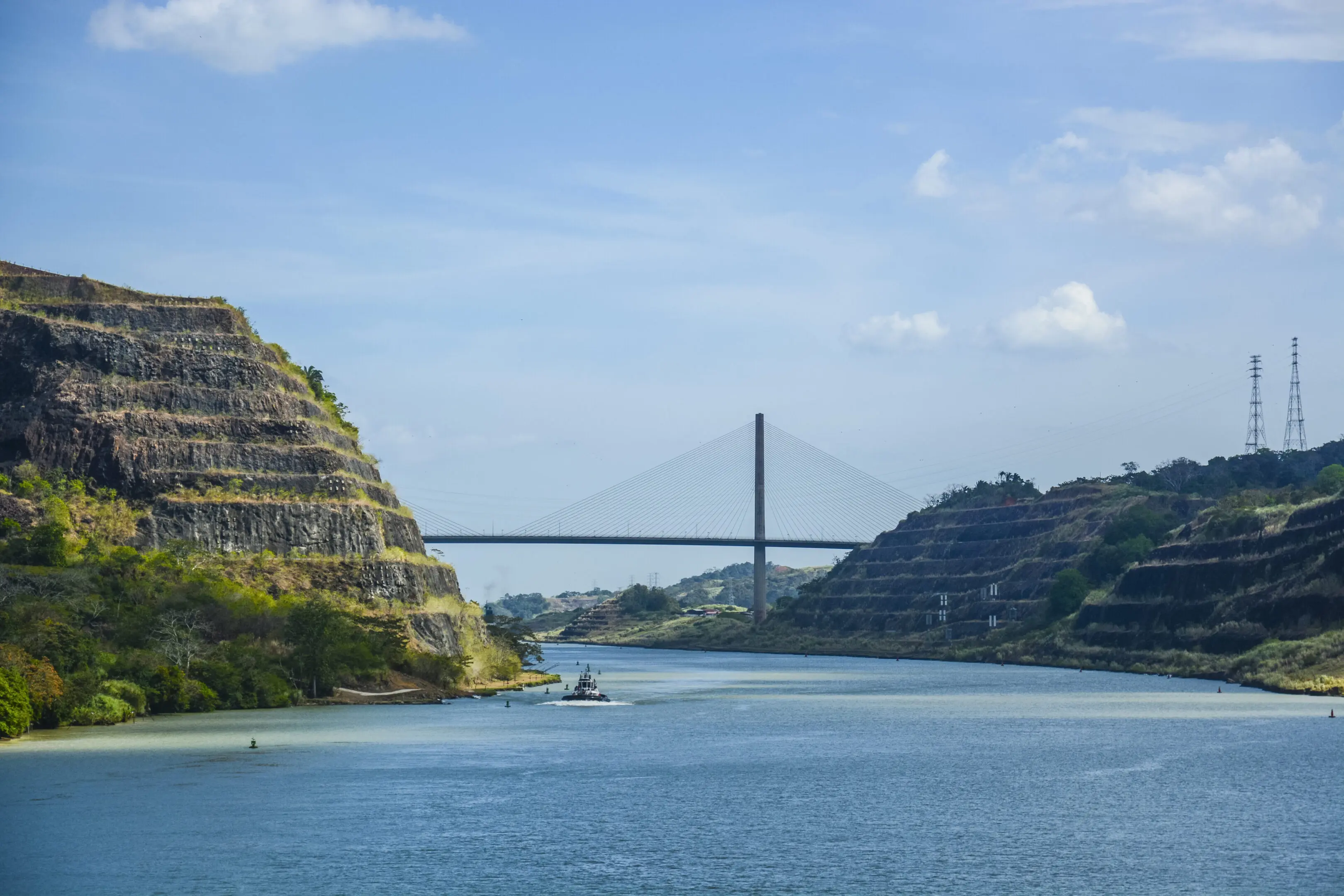 Centennial Bridge, Panama Canal A boat is traveling down the river near some mountains.