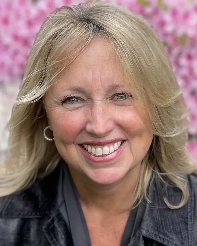 A woman with blonde hair and blue eyes smiling.